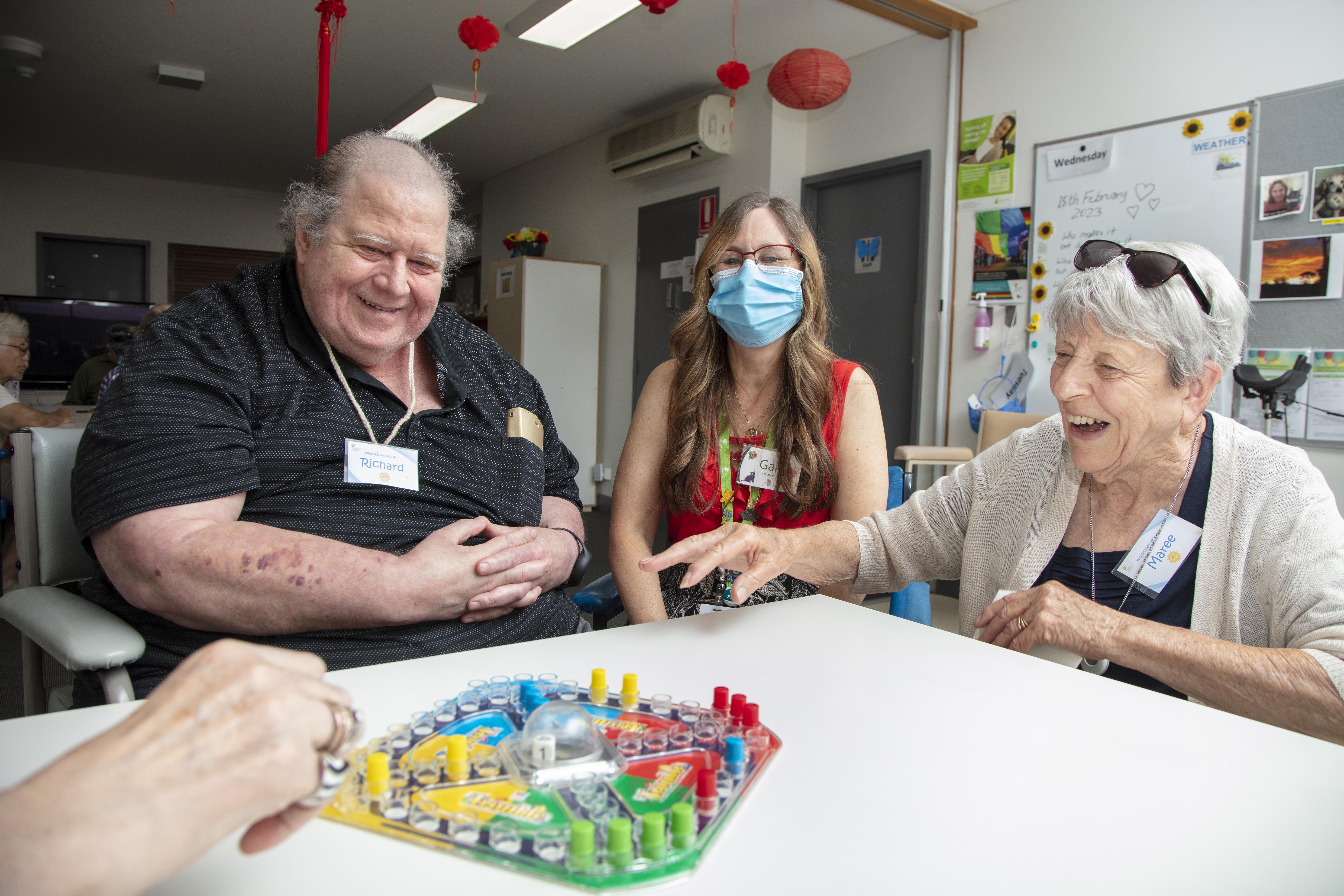 Two Connect Well participants sit and play games with a volunteer worker