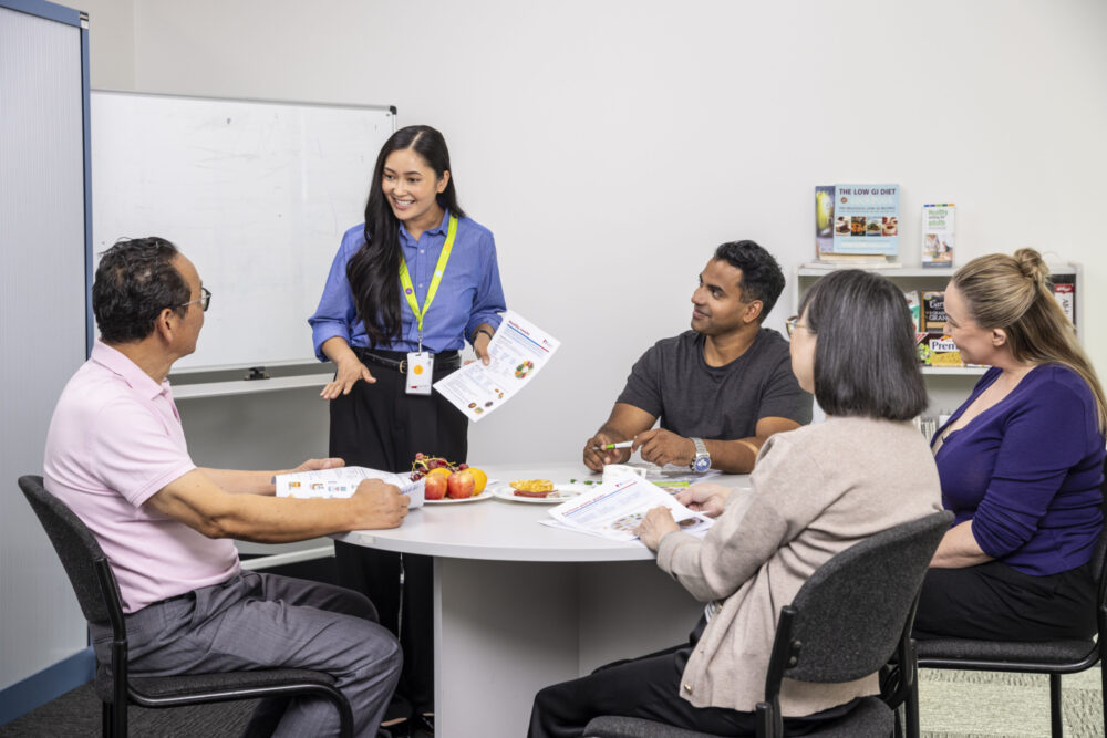 A health practitioner talks to a group of people seated around a table